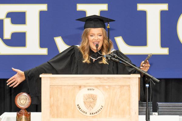 学生罗西·卢克穿着毕业礼服站在讲台上，张开双臂庆祝